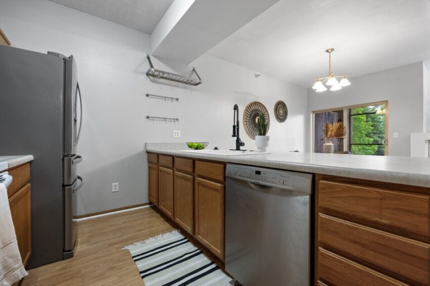 Modern kitchen with wooden cabinets, stainless steel appliances, and a striped rug.