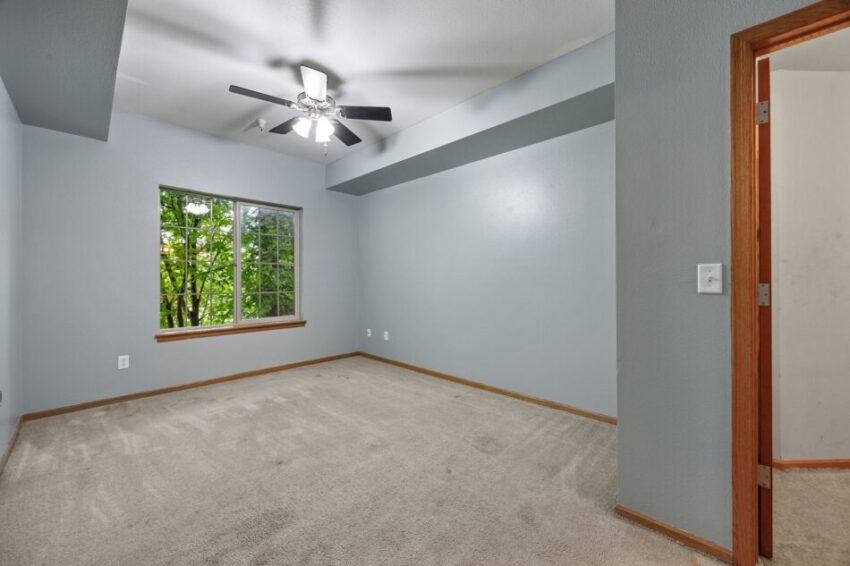 Bedroom with gray walls, beige carpet, window, and ceiling fan.