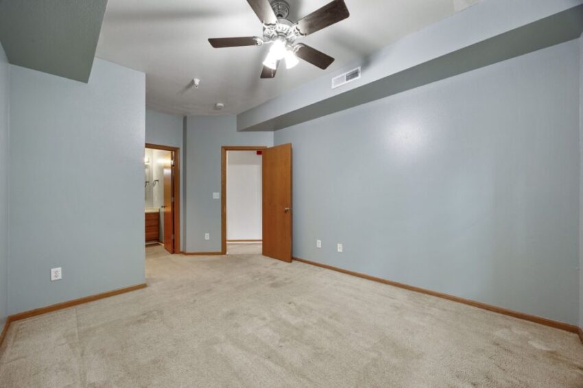 Bedroom with beige carpet, gray walls, ceiling fan, and open door to bathroom.