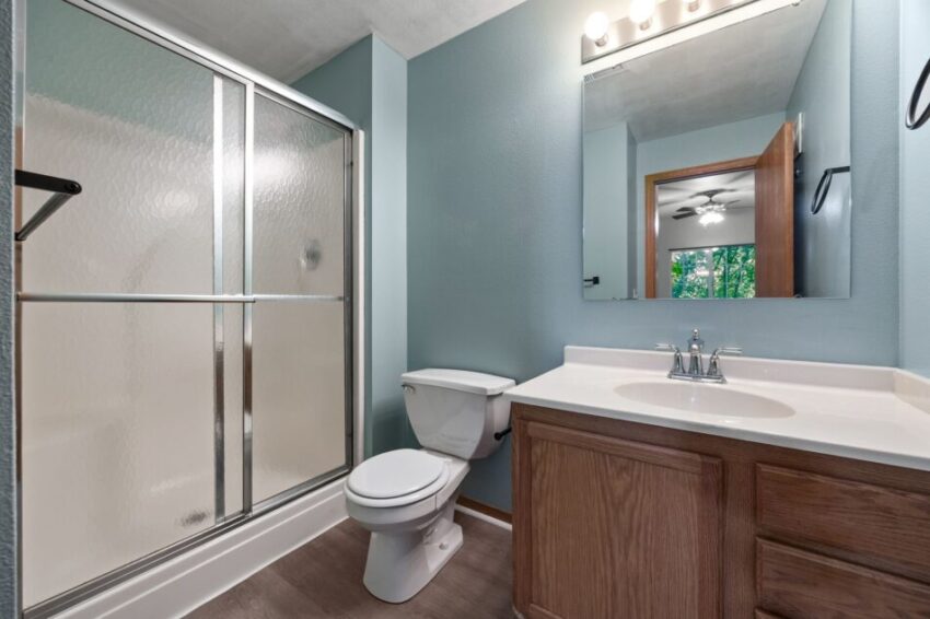 Bathroom with shower, toilet, and wooden vanity under bright lighting.