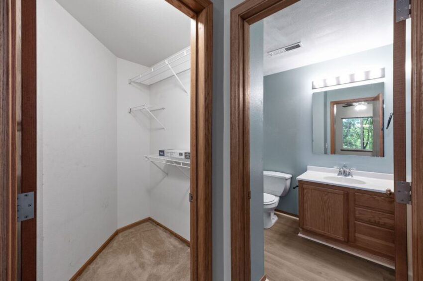 Closet with wire shelving and bathroom with wooden cabinets and large mirror.