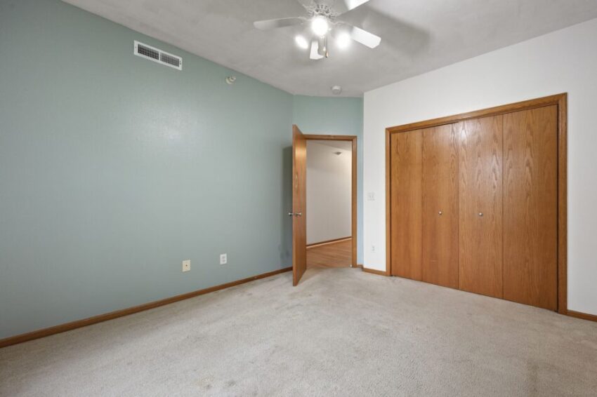 Bedroom with green and white walls, ceiling fan, and wooden closet doors.