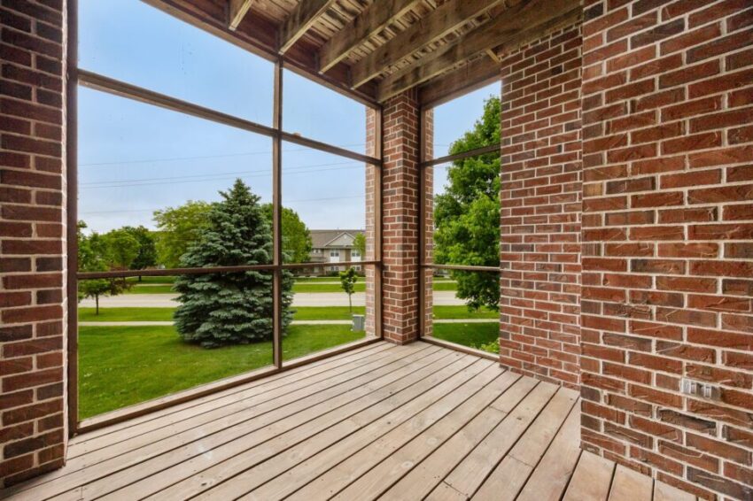 Brick balcony with wooden floor, overlooking trees and a street.