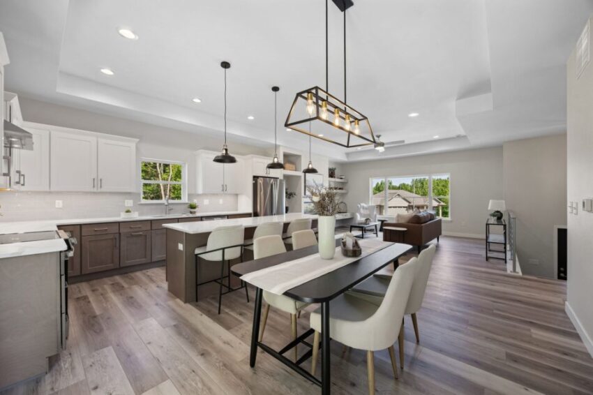 Modern kitchen with island, dining table, and large windows overlooking a green lawn.