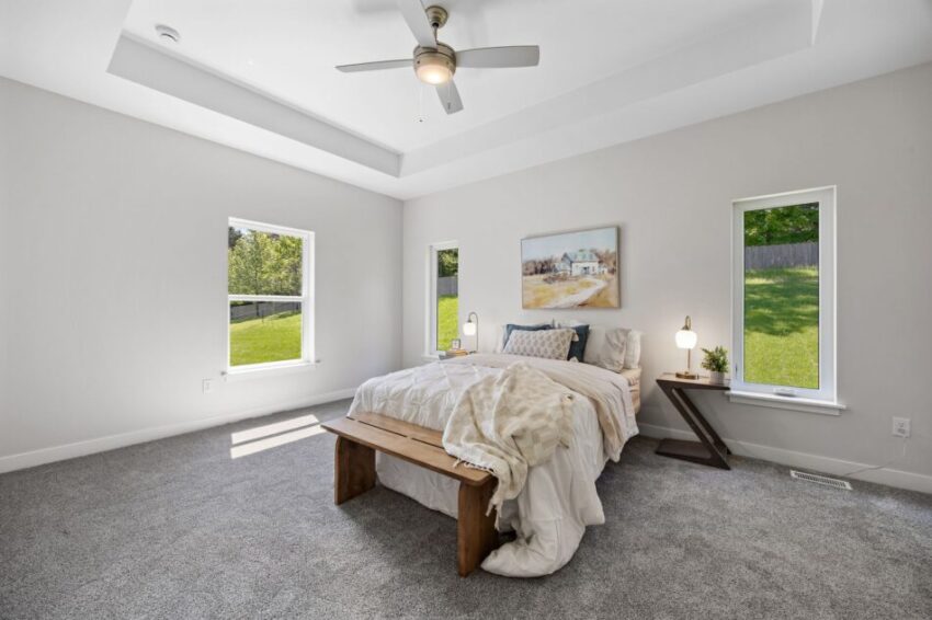 Bright bedroom with a bed, bench, and two windows overlooking a green yard.