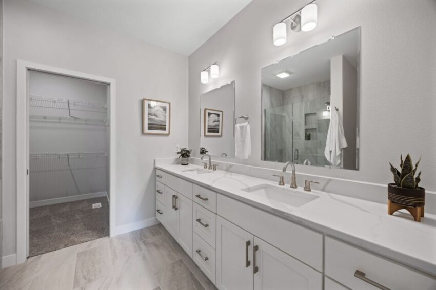 Modern bathroom with double sinks, large mirror, and walk-in closet.