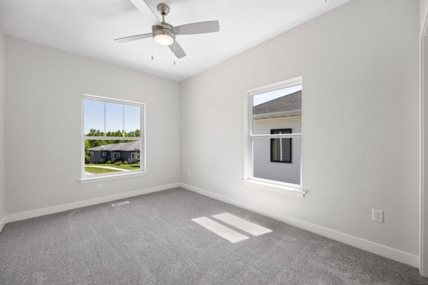 Bedroom room with gray carpet, white walls, and two windows. Ceiling fan overhead.