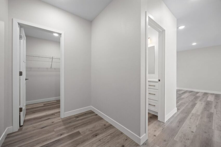 Hallway with gray walls, open doors, and wood-toned flooring.
