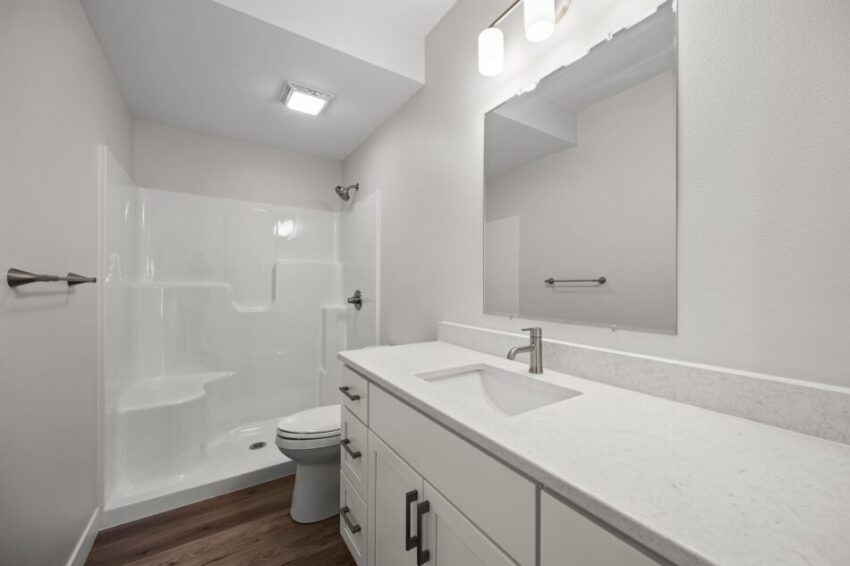 Modern bathroom with white fixtures, shower, and wooden floor.