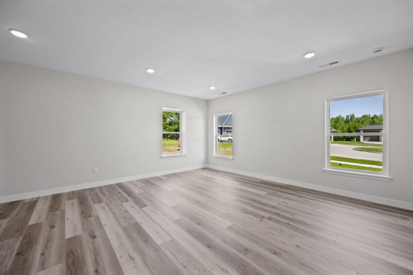 Lower level room with light wood flooring and three windows.