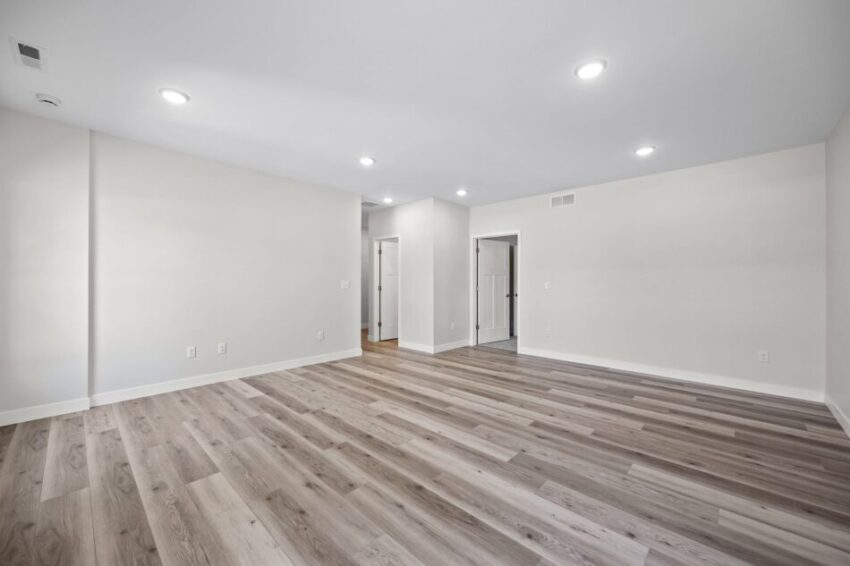 Lower level room with light wood flooring and three windows.