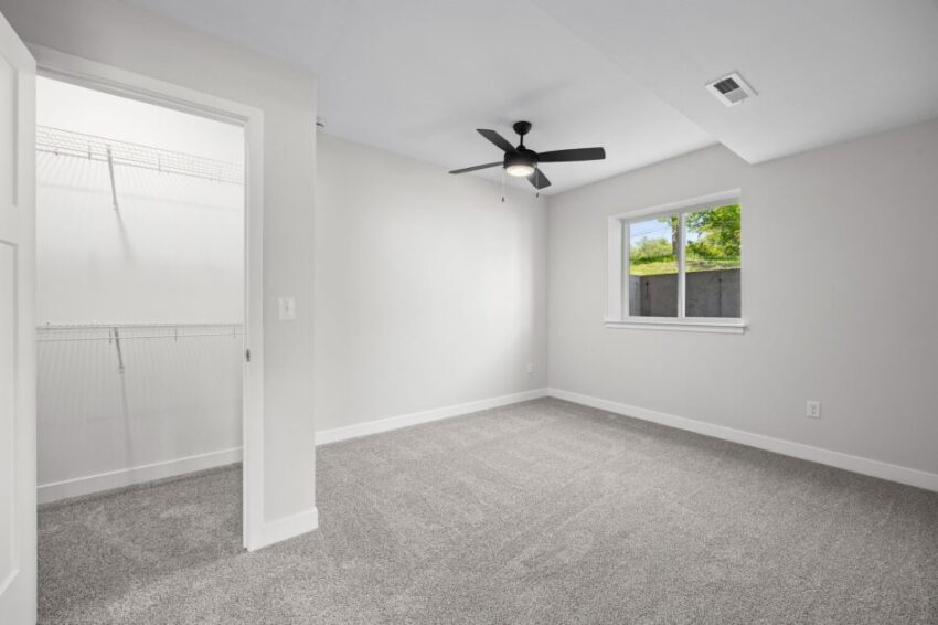 Bedroom with gray carpet, ceiling fan, and open closet door.