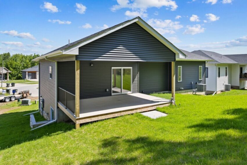 Back yard view of a modern house with a wooden deck and sliding glass doors.