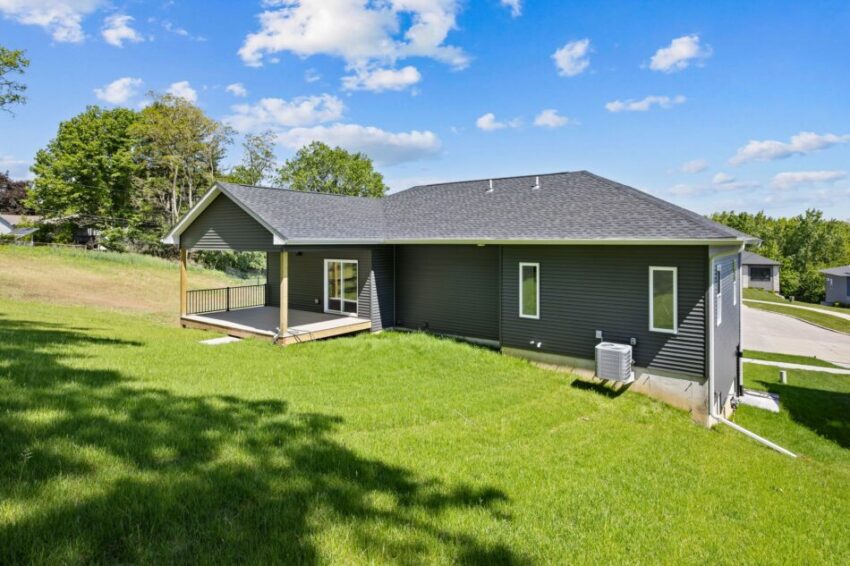 Single-story house with a dark exterior and a spacious green lawn.