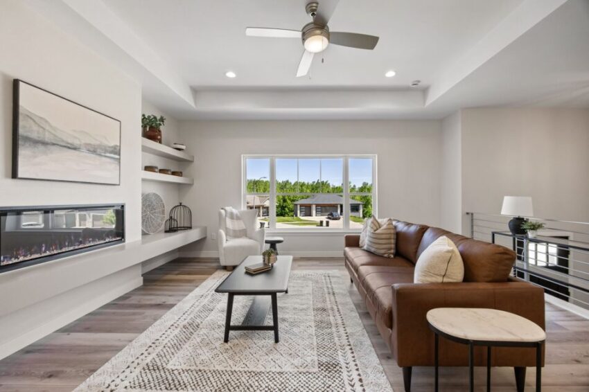 Modern living room with fireplace, large window, and ceiling fan.