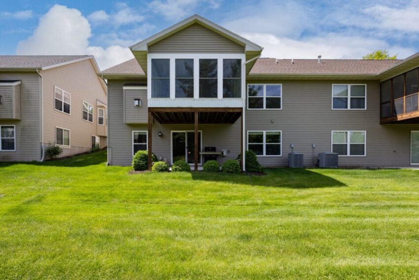 Backyard view of a two-story house with green lawn and large windows.
