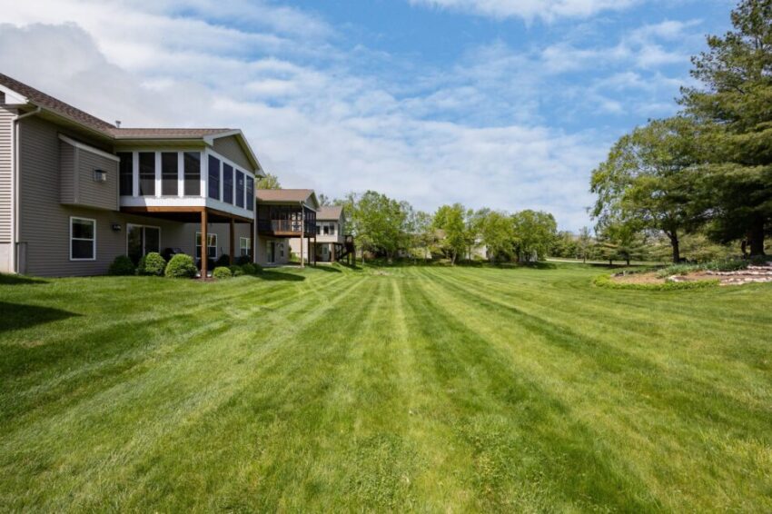 Houses with large green lawn and trees under a blue sky.