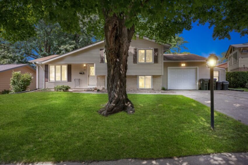 Suburban house with a tree in front, illuminated at dusk.