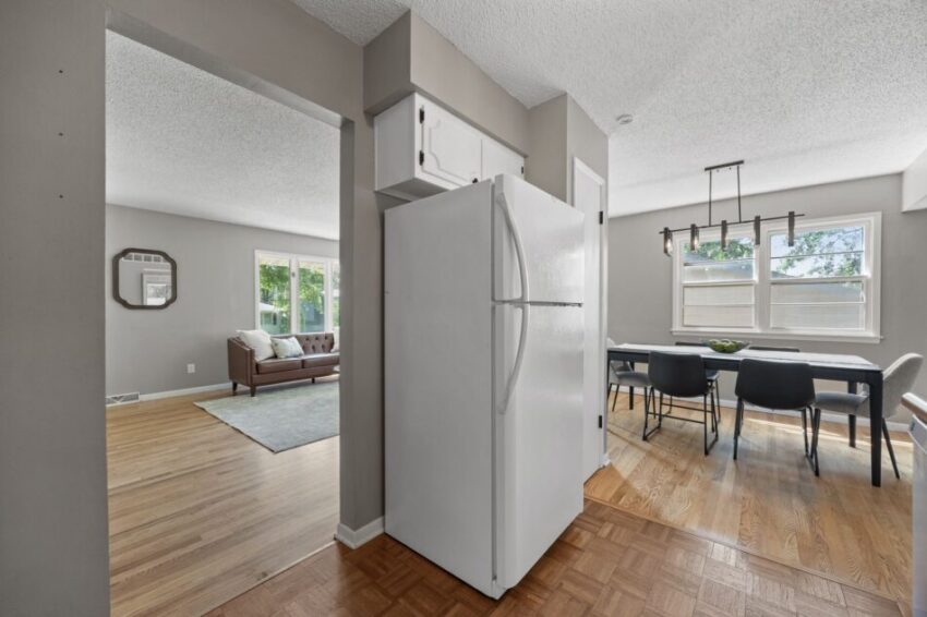 Open kitchen and dining area with white refrigerator and wooden floors.