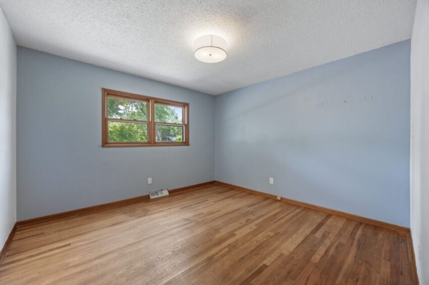 Empty room with wooden floor, blue walls, and a window.