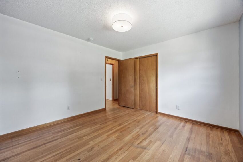 Empty room with wooden floor and closed wooden closet doors.