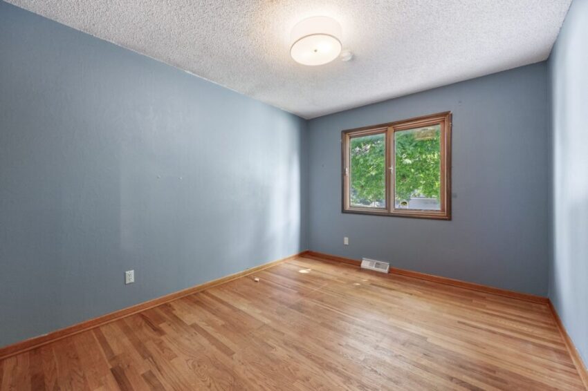 Empty room with blue walls, wooden floor, and a window.