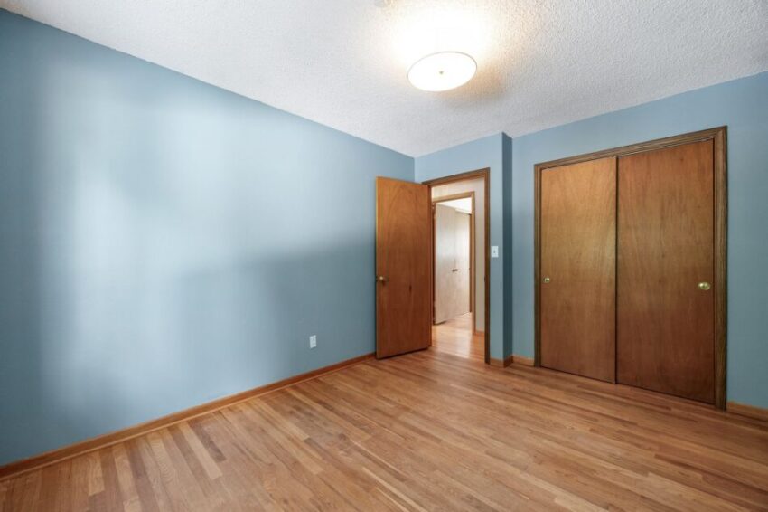 Empty room with blue walls, wooden floor, and closed wooden doors.