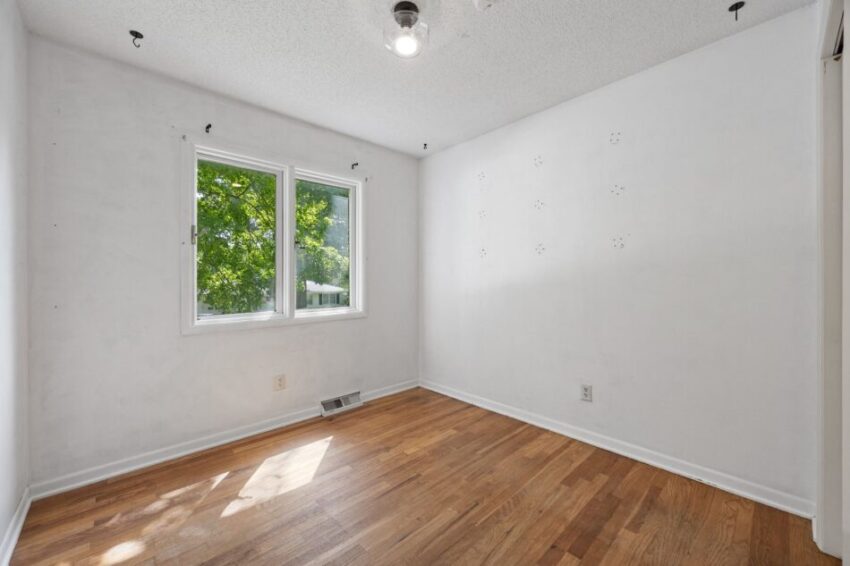 Empty room with wooden floor, white walls, and two windows.