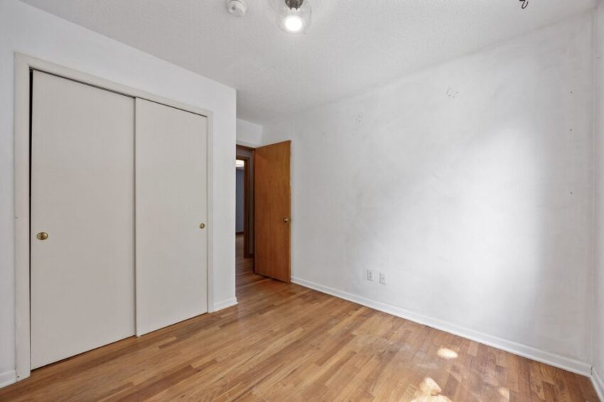 Empty room with wooden floor, white walls, and closed closet doors.