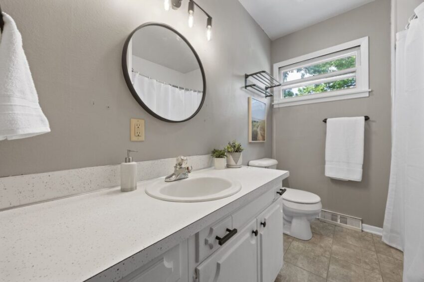 Modern bathroom with round mirror, white countertop, and towel rack.