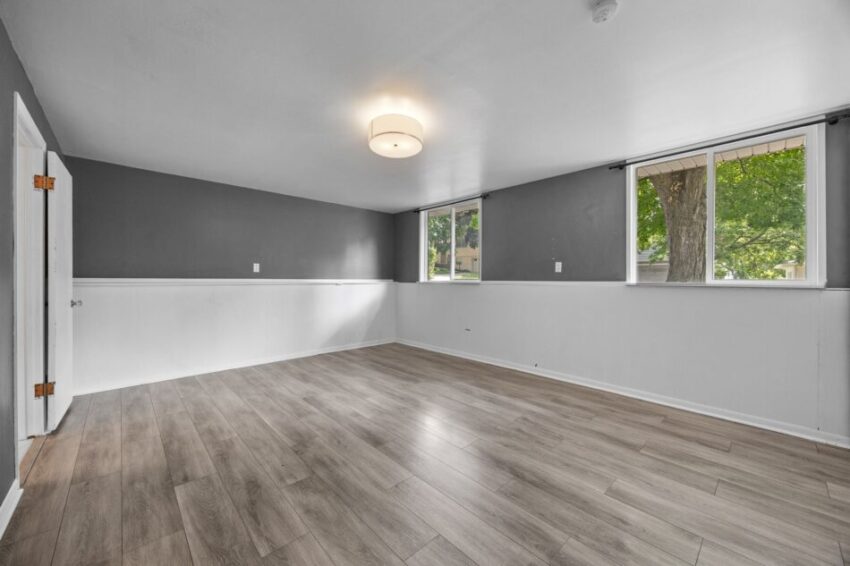 Empty room with gray walls, wood flooring, and two windows.