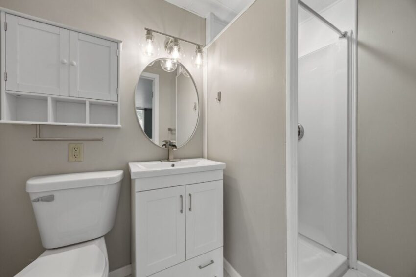 Modern bathroom with white fixtures and round mirror.