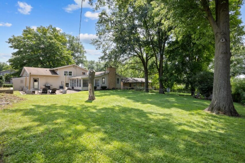 Spacious backyard with trees and a house under a clear blue sky.