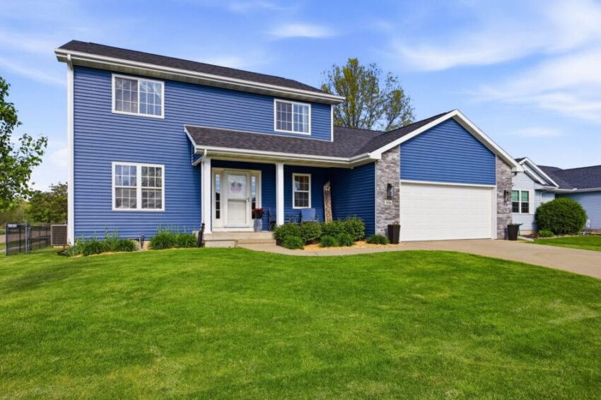 Two-story blue house with attached garage, green lawn, and clear sky.