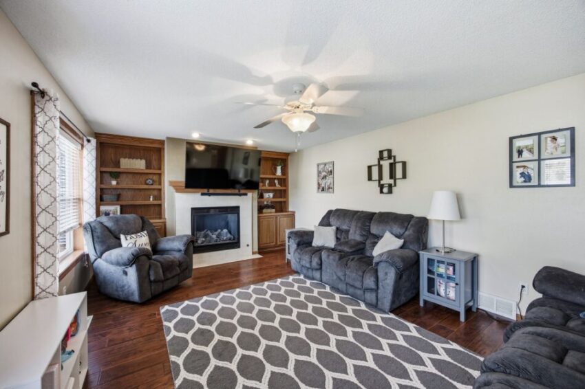 Living room with mounted TV above fireplace, wooden shelves, and cabinets on both sides.
