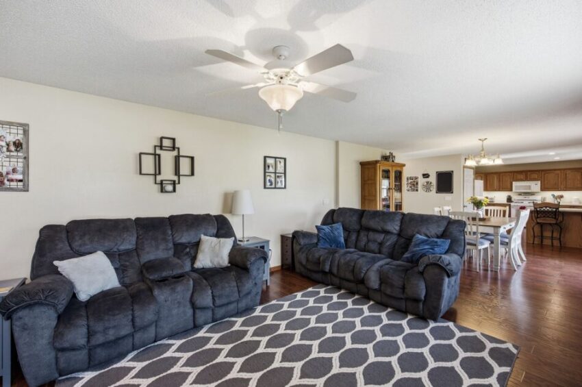 Living room with two gray sofas, patterned rug, ceiling fan, and view into dining and kitchen area.