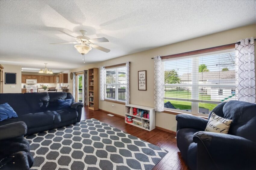 Bright living room with large windows, blue sofas, patterned rug, and view of backyard.