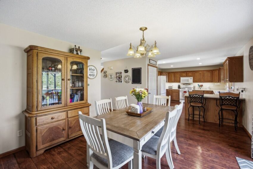 Spacious dining area with wooden table, white chairs, china cabinet, and open kitchen in background.