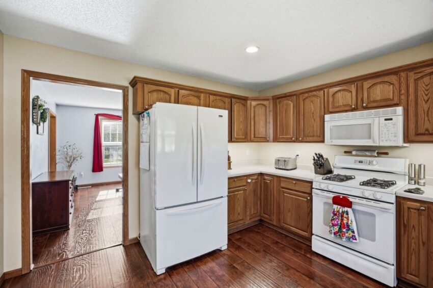 Kitchen with wooden cabinets, white appliances, and hardwood floor, adjacent to a sunlit dining room.