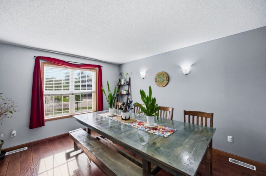 Dining room with wooden table, bench seating, plants, large window, and gray walls.