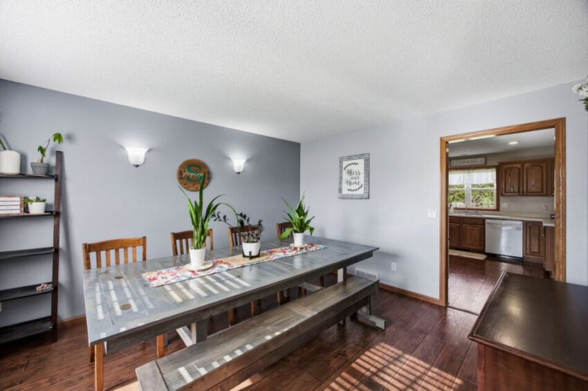 Dining room with long table, wooden chairs, bench seating, plants, and view into kitchen.