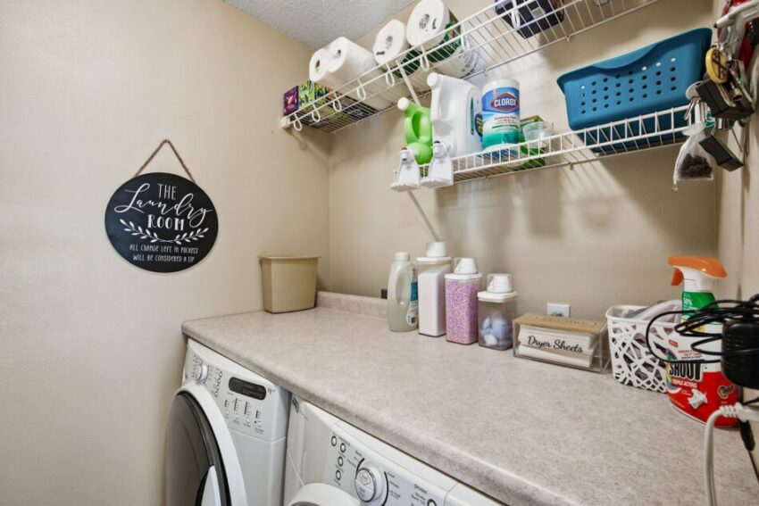 Laundry room with washer, dryer, countertop, cleaning supplies, and wall shelf holding paper towels.