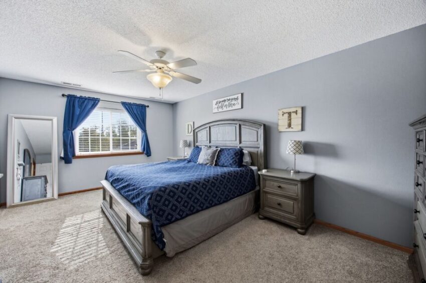 Spacious bedroom with blue walls, large bed, nightstands, dresser, window, and ceiling fan.