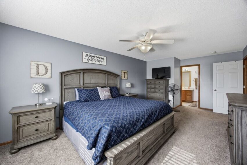 Spacious bedroom with king bed, blue bedding, wooden furniture, ceiling fan, and natural light.