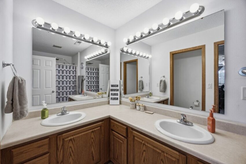 Double bathroom vanity with mirrors, bright lighting, soap dispensers, and a motivational sign.