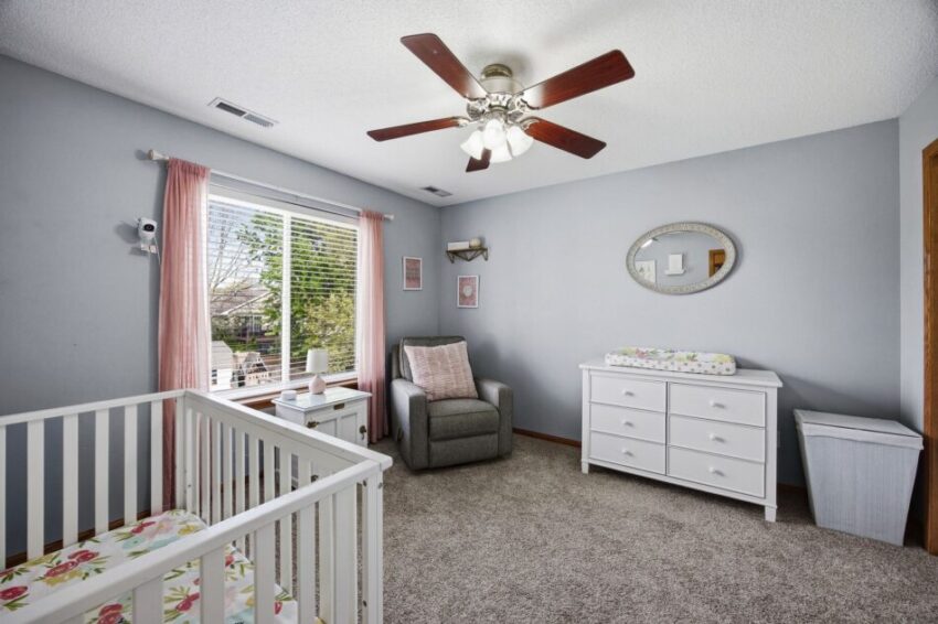 Nursery room with crib, changing table, armchair, ceiling fan, and window with natural light.