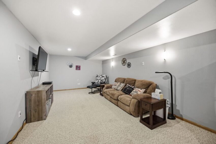 Spacious basement living room with beige carpet, brown sofa, TV, and wall decor.