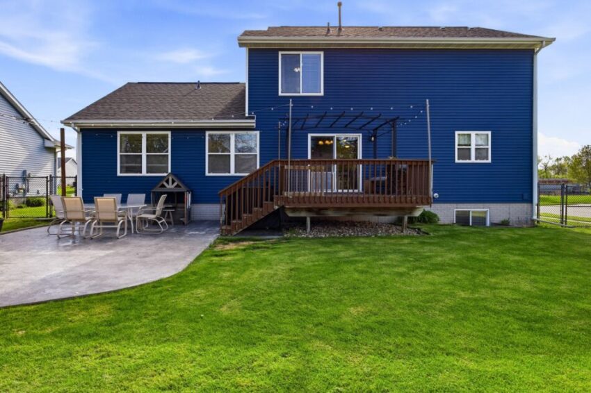 Blue house with wooden deck, patio furniture, and green lawn under a clear sky.